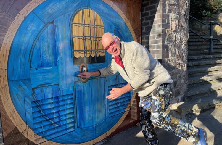 Man poses with life size painting of blue Hobbit door