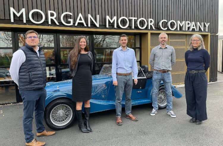 five people stand in front of a Morgan car