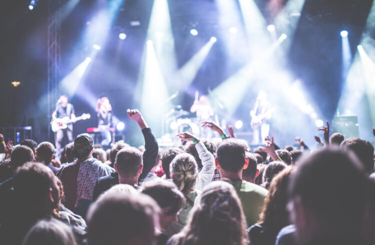 A crowd of people in front of a band playing on a stage at a festival.