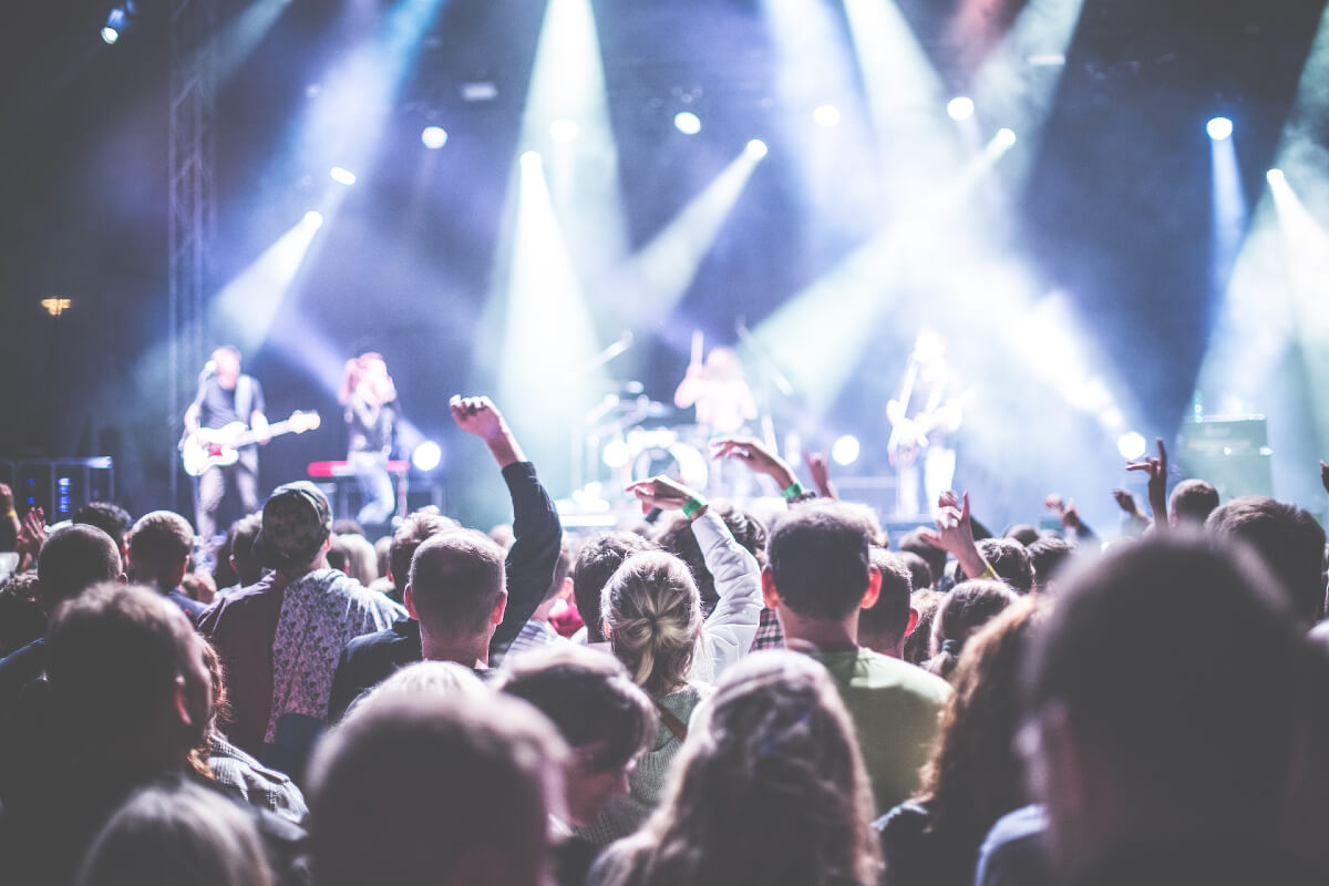 A crowd of people in front of a band playing on a stage at a festival.