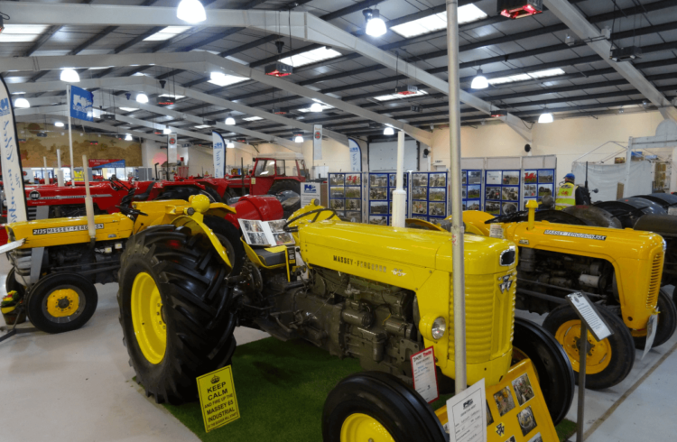 A warehouse full of tractors with a bright yellow tractor in the foreground