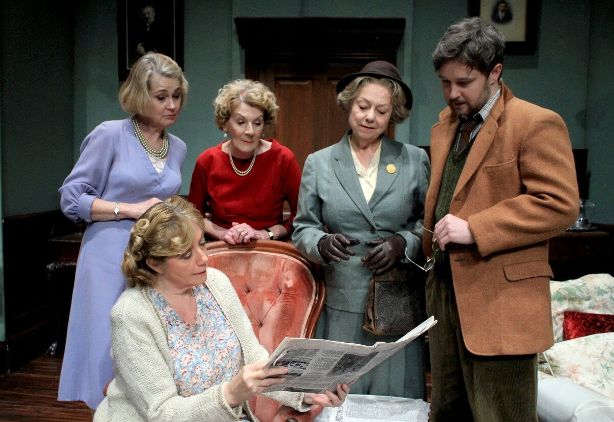 Four women including Miss Marple and one man study a newspaper