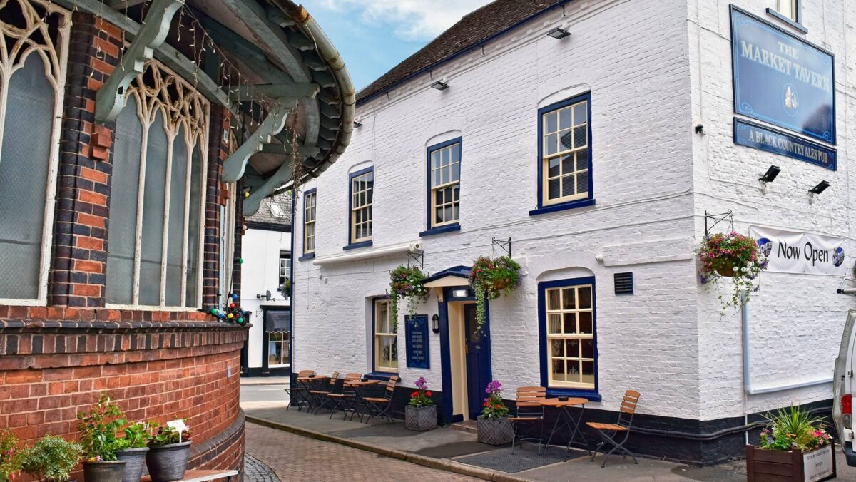 Exterior of the pub, featuring sash windows, painted brickwork, hanging baskets and outdoor seating