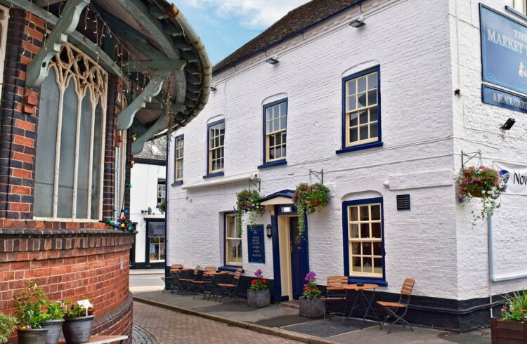 Exterior of the pub, featuring sash windows, painted brickwork, hanging baskets and outdoor seating