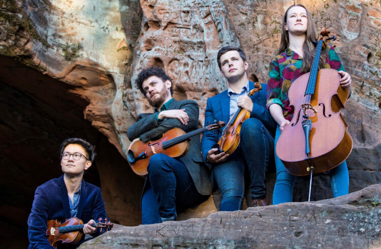 4 musicians holding 3 violins and 1 cello stood on a rock