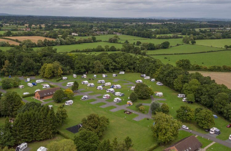 Aerial view of a caravan site with tree edged fields and white campervans in the park