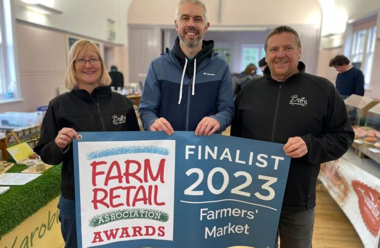 Three people hold a banner at a farmers market