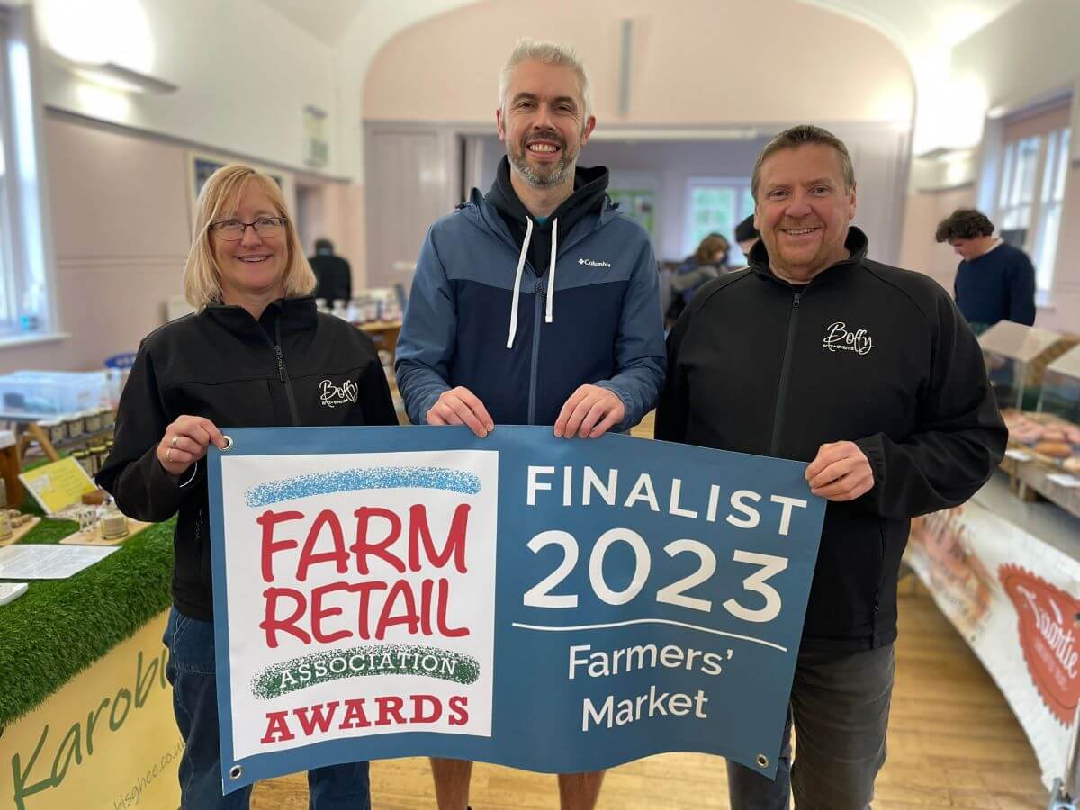 Three people hold a banner at a farmers market