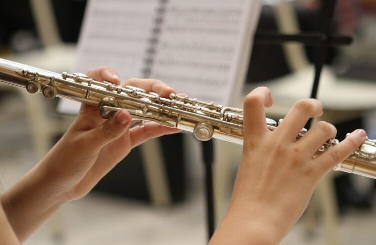 A woman playing a flute with a music stand in the background