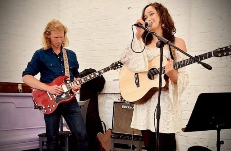 Two people play guitar and one also sings onstage