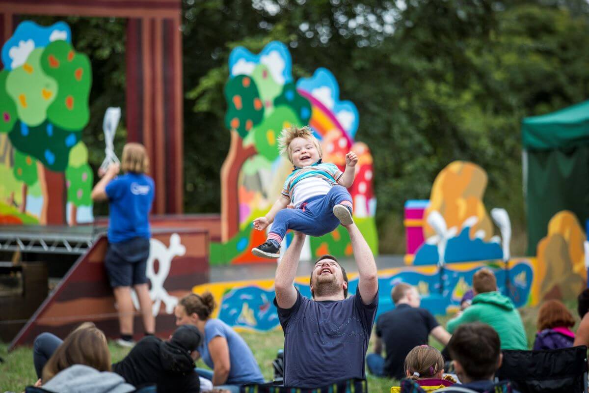 Families play outside and a man throws his son in the air playfully