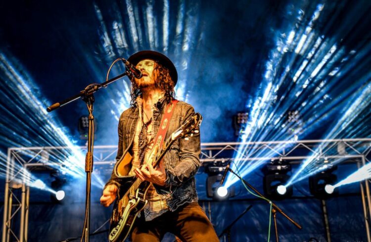 A man plays electric guitar and sings onstage with stage lights in the background