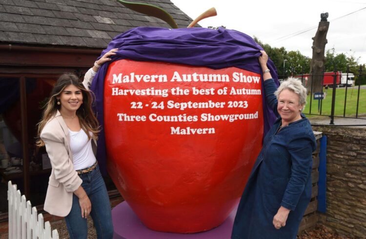 Two people unveiling a giant red apple