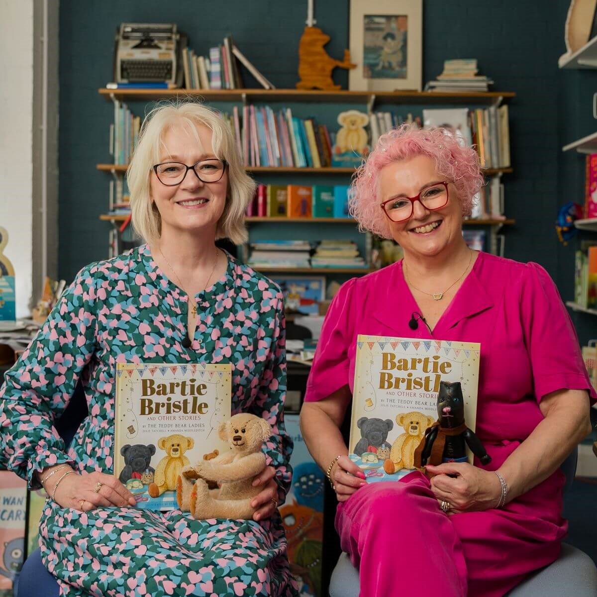 Two authors hold their book and a teddy bear. They are smiling warmly.