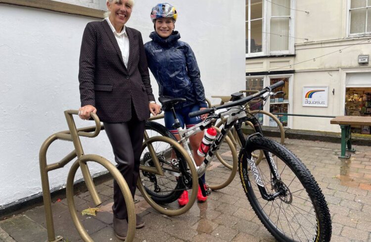 One cyclist and one person pose with golden painted bike racks shaped like bikes