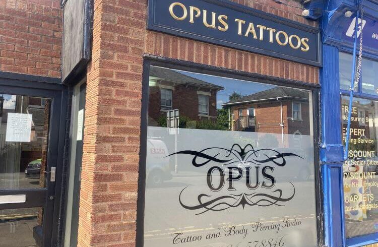 A shop front with brick, large window and blue and gold sign