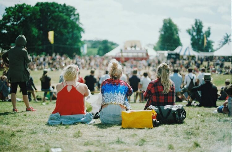 Three people sat on the grass at a music festival