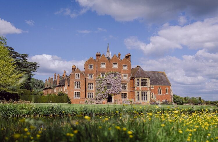 Front view of Elizabethan Madresfield Court with blue sky above and flowers and lawns to the front