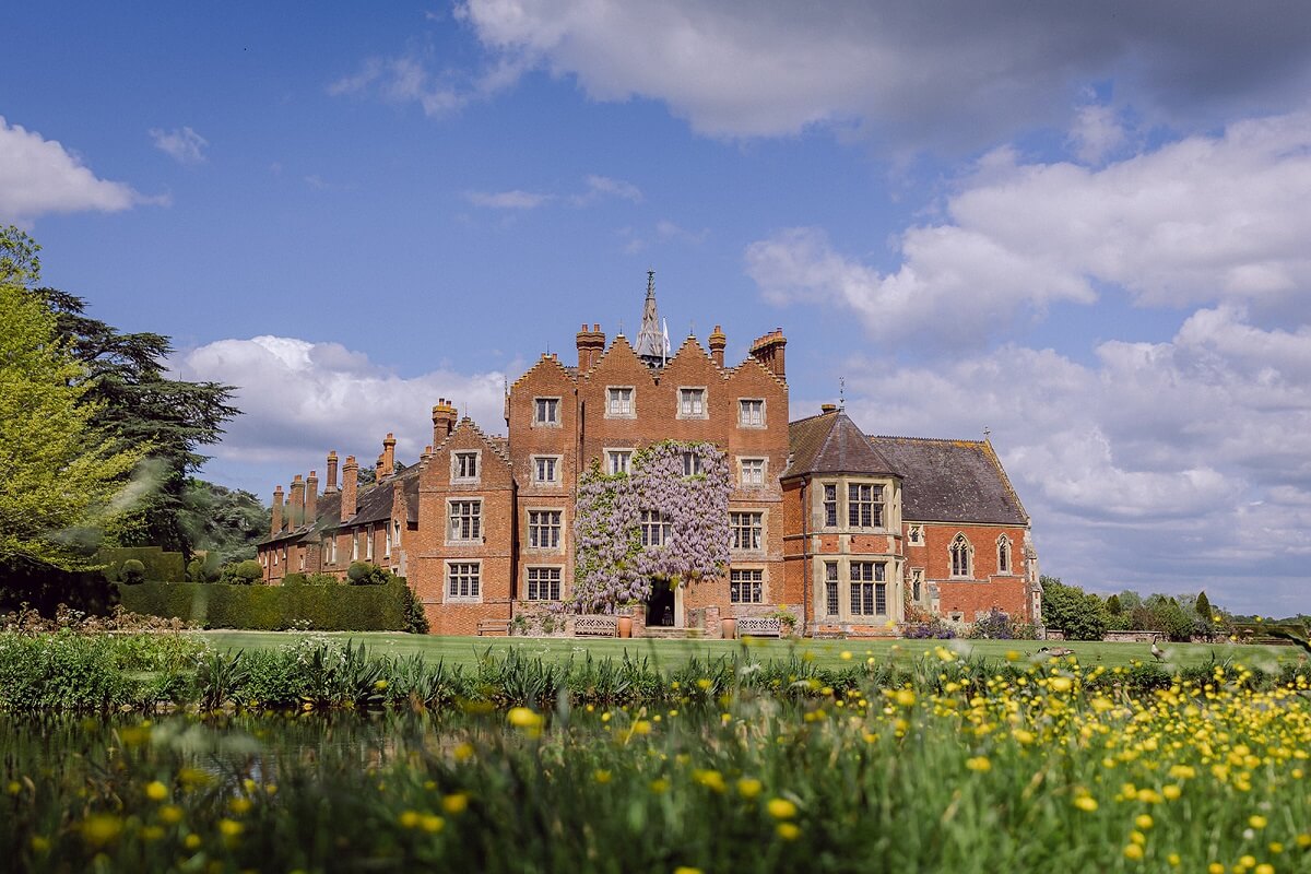 Front view of Elizabethan Madresfield Court with blue sky above and flowers and lawns to the front