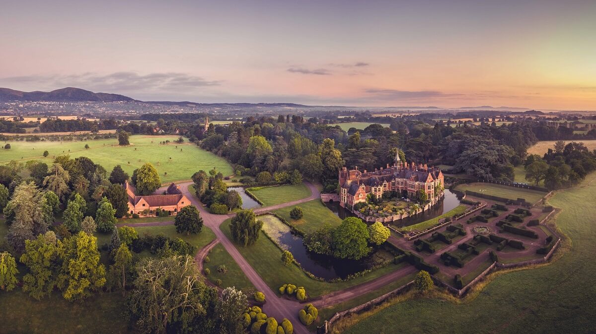 Aerial view of Madresfield Court with moat and gardens and outline of Malvern Hills in background