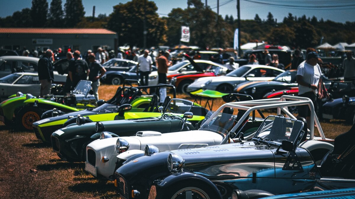 Kit cars of various colours and types lined up in a field with visitors walking around to see the cars