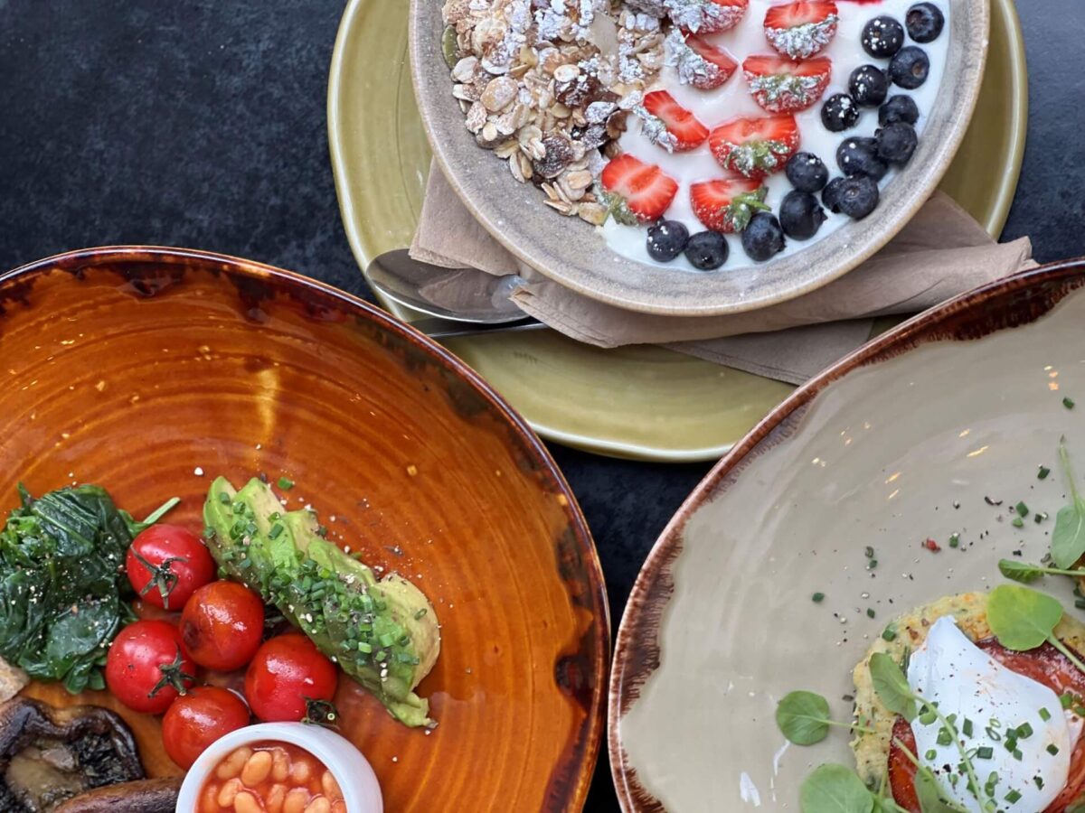 Three plates of breakfast food: granola, poached eggs and a full veggie breakfast