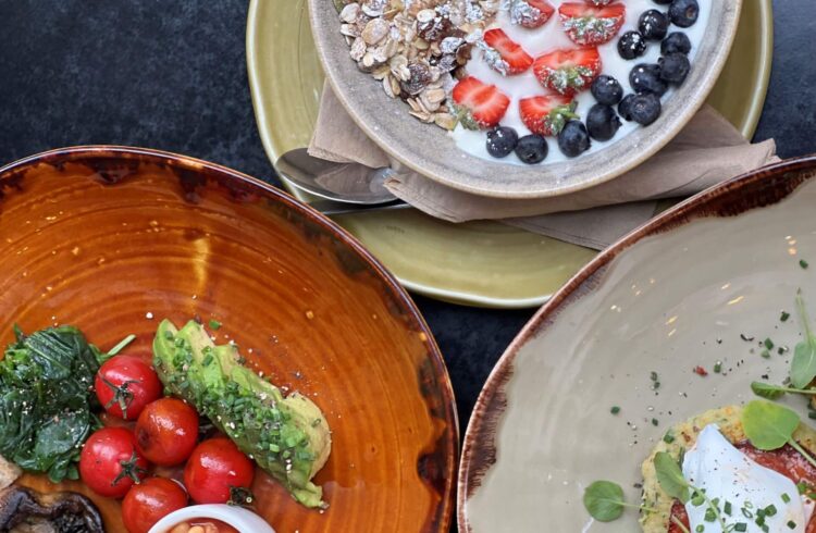 Three plates of breakfast food: granola, poached eggs and a full veggie breakfast