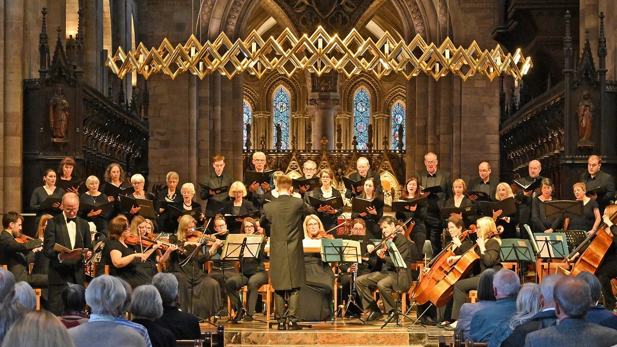 An audience watching a classical orchestra playing, with smartly choral singers behind