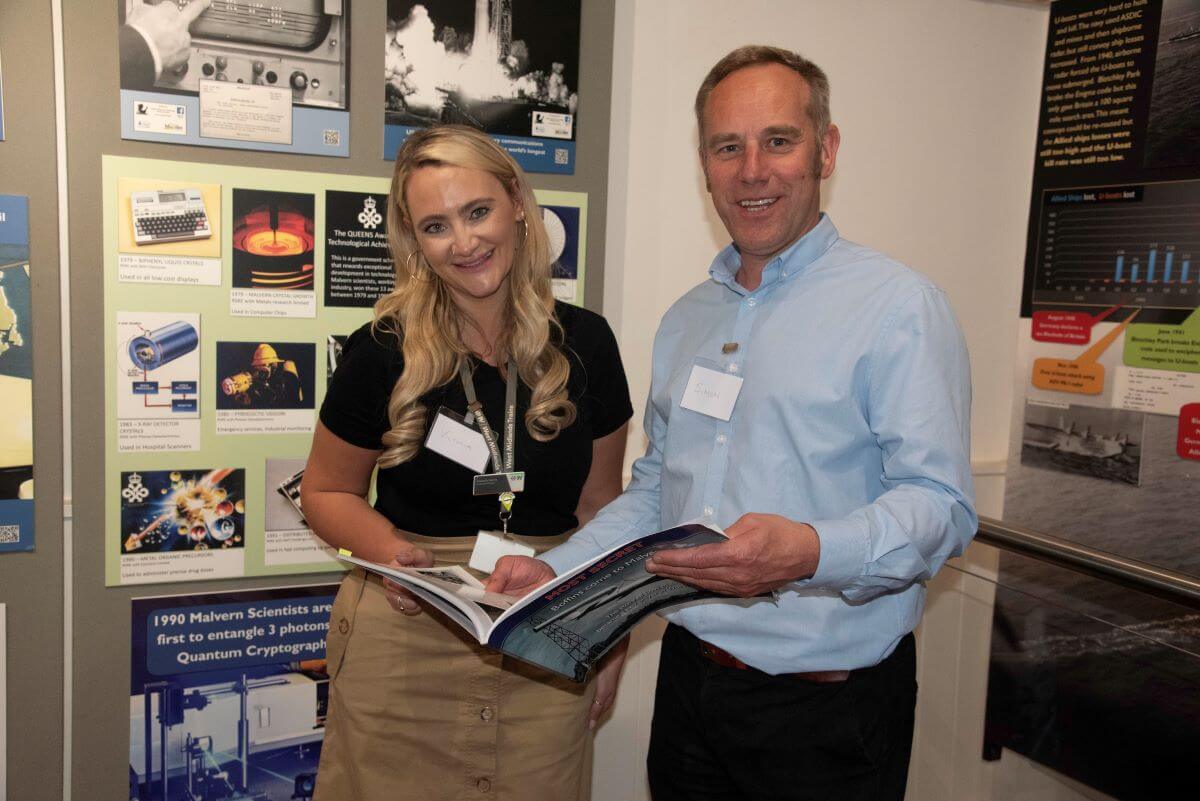 Two people read a leaflet and smile in front of a museum display