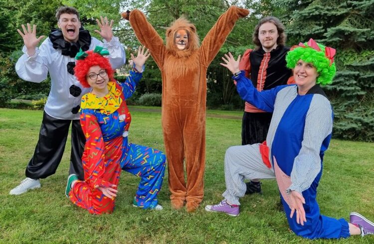 Five actors, in costume, smile at the camera during rehearsals for 'The Lion That Lost Its Roar' (actors named in main text)