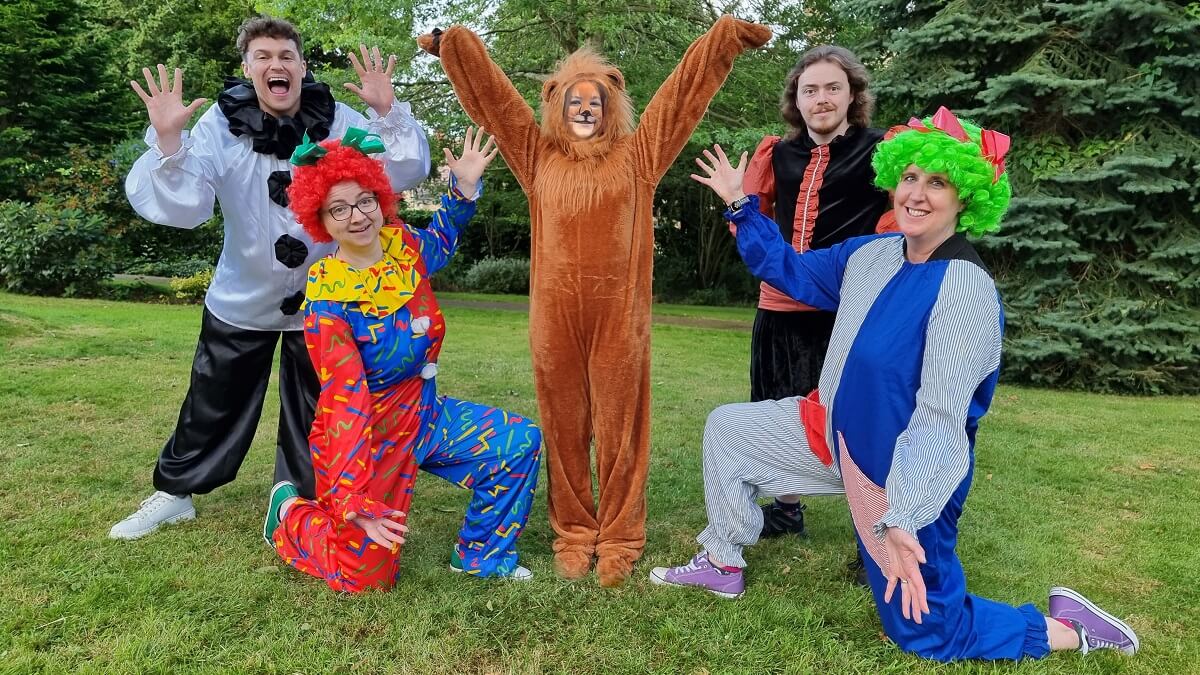 Five actors, in costume, smile at the camera during rehearsals for 'The Lion That Lost Its Roar' (actors named in main text)