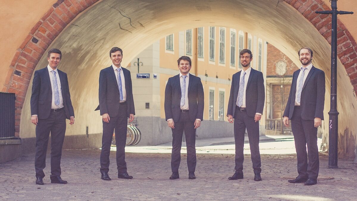 The five members of the group all wearing matching suits and ties