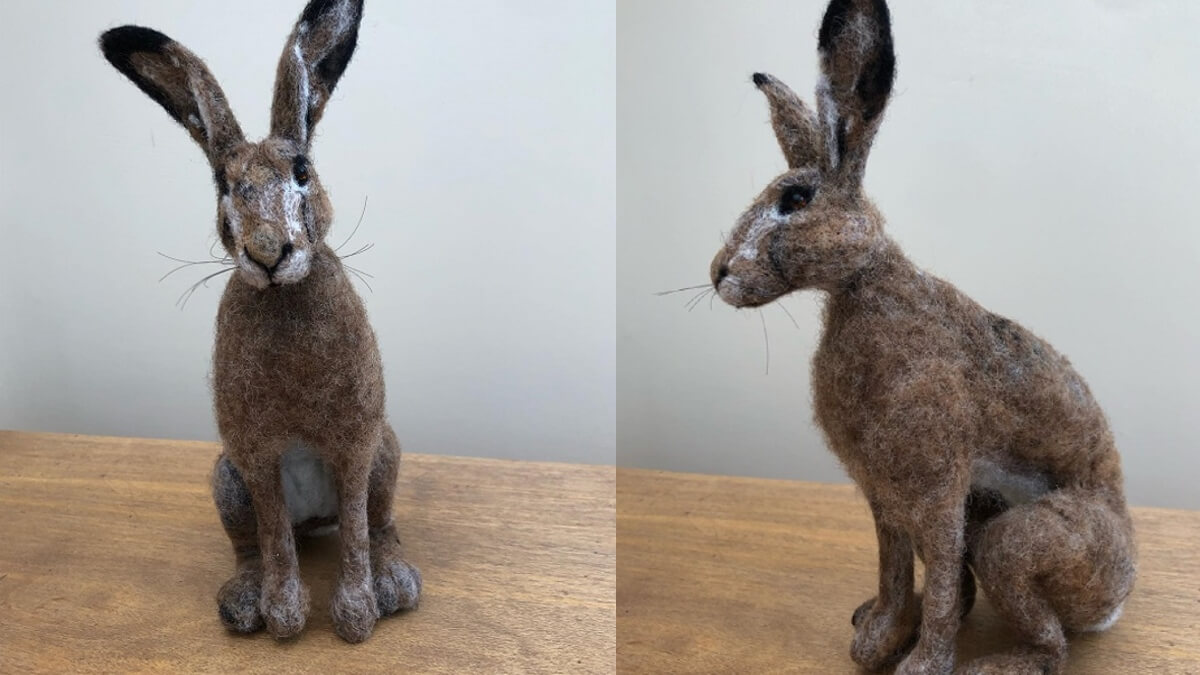 A needle felted hare displayed on a wooden table against a grey background