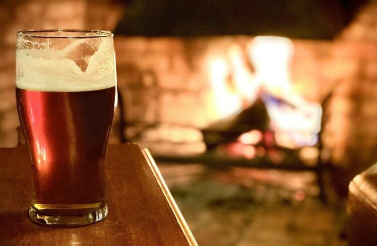 A pint of beer on a wooden table with open fire in background