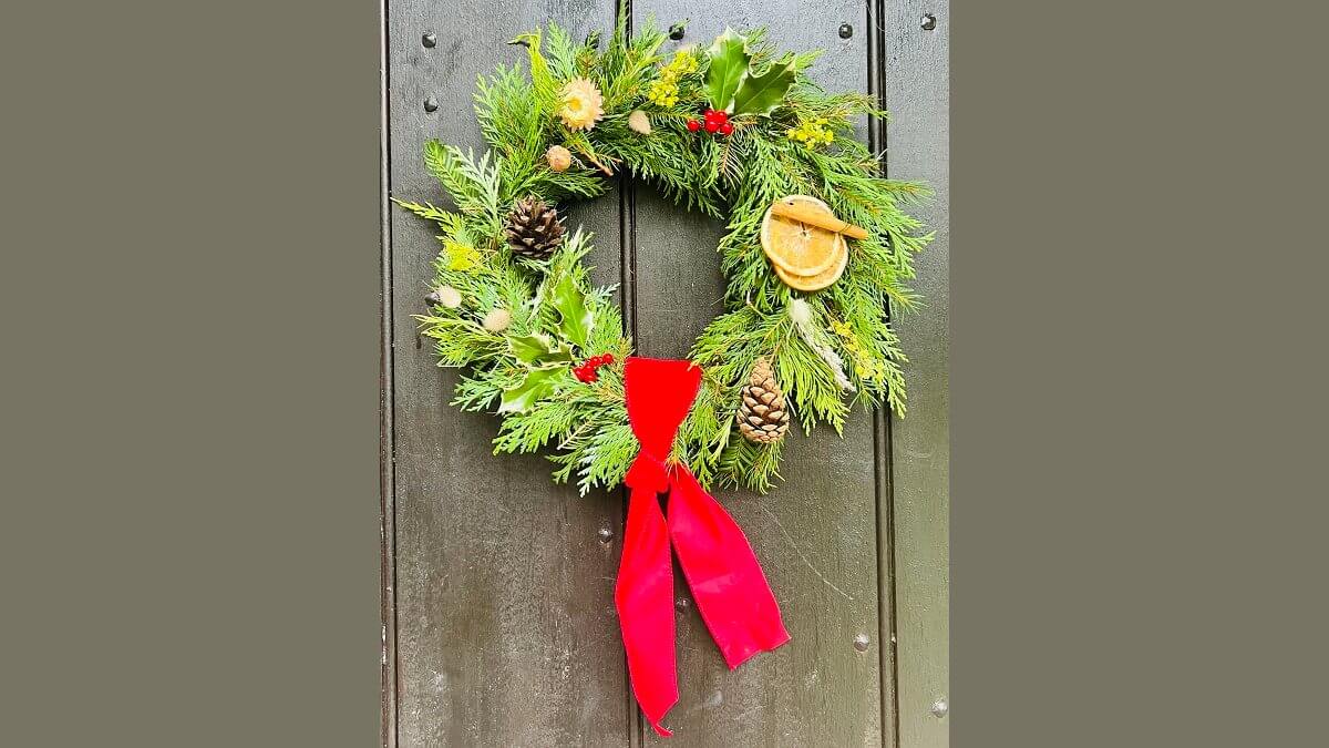 A Christmas wreath featuring foliage, cones, holly on a green door