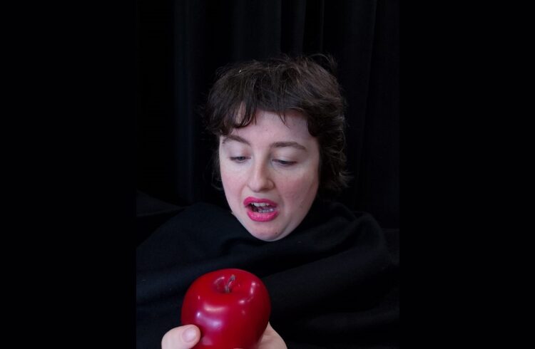 A woman, dressed in black, looking at a red apple